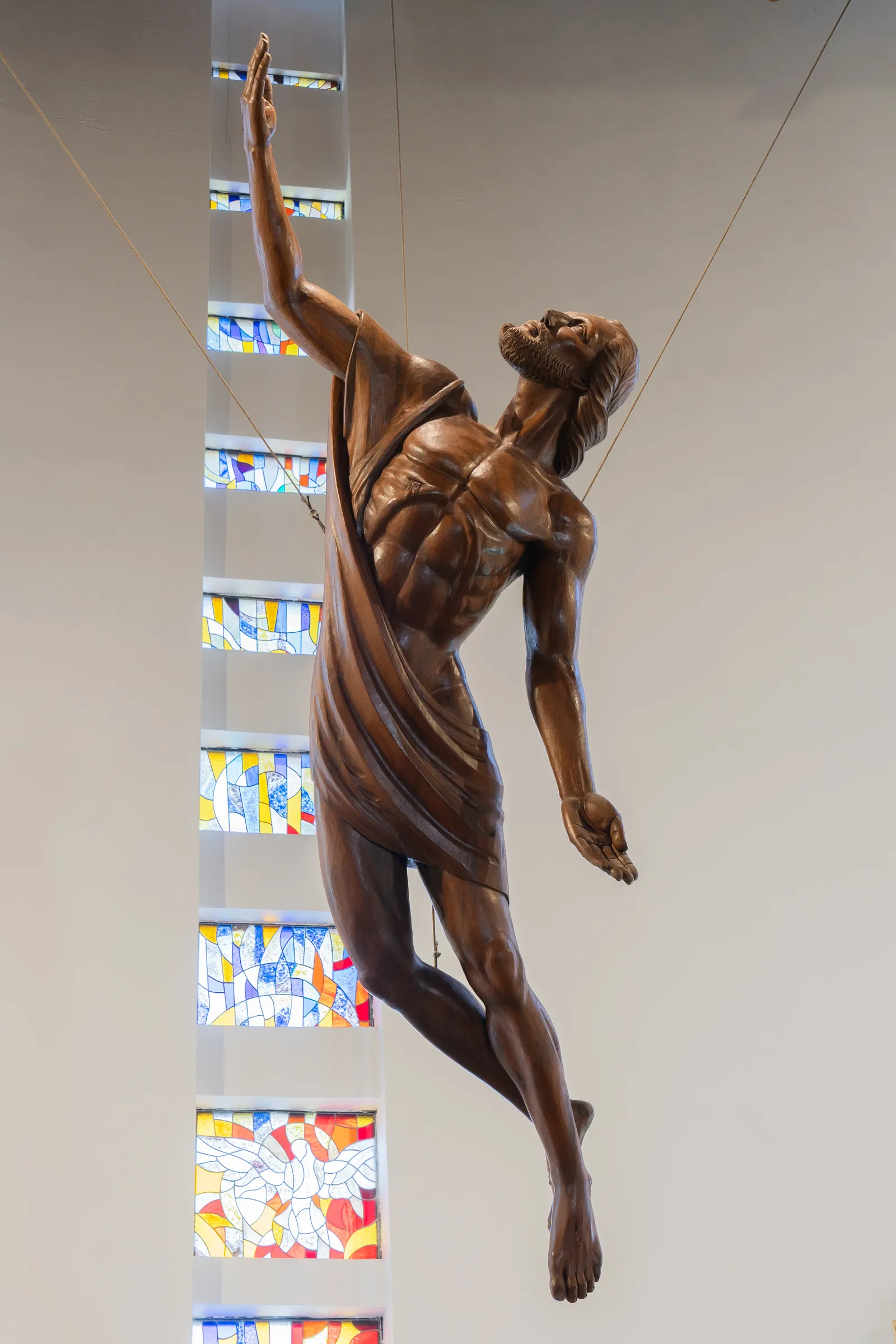 Figura en bronce suspendida en el interior de una iglesia, ante los vitrales